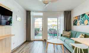 Et lyst opholdsrum med en grøn sofa, et sofabord og udsigt til en terrasse gennem en glasdør. (AI-genereret tekst)