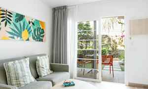 Stuemiljø med grå sofa, puder, farverigt vægkunst og glasdør, der fører til terrasse. (AI-genereret tekst)