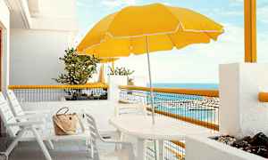 Hvid terrasse med stole, bord, gul parasol og havudsigt. (AI-genereret tekst)