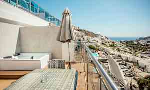 En altan med siddeområde og udsigt over en by og havet. (AI-genereret tekst)