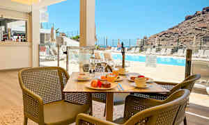 Et bord med morgenmad og stole foran en pool og bjerge i baggrunden. (AI-genereret tekst)