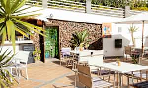 Terrasse med borde, stole og parasol nær en bygning med stenvæg. (AI-genereret tekst)