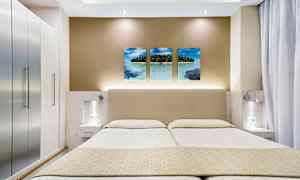 Billedet viser et moderne hotelværelse med en dobbeltseng, stilfulde sideborde og vægdekoration med tre billeder af et tropisk strandmotiv. (AI-genereret tekst)