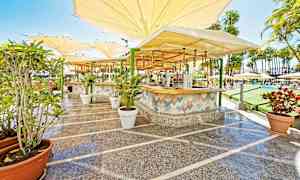 Udendørsmiljø med en bar og siddepladser under store parasoller. (AI-genereret tekst)