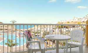 Udsigt fra en altan med hvide møbler mod en pool og en havudsigt. (AI-genereret tekst)