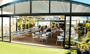 Billede af en restaurant med siddeområde udendørs og glasvægge. (AI-genereret tekst)