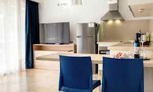 Et køkken med en køkkenbord, to blå stole, et køleskab og et fjernsyn ved et træskab. (AI-genereret tekst)