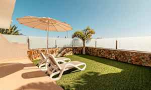 En udendørs terrasse med to liggestole, parasol og kunstgræs. (AI-genereret tekst)