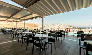 Udendørs serveringsområde med borde og stole, udsigt over by og hav. (AI-genereret tekst)