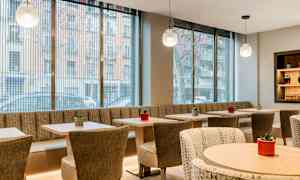 En moderne og lyst indrettet café med store glasvinduer, borde og stole samt små planter som dekoration. (AI-genereret tekst)