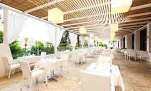 Restaurant med hvide borde og stole under tag nær grønne områder. (AI-genereret tekst)