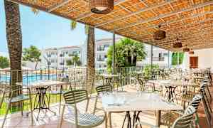 Terrasse med borde og stole, en pool og hotelbygninger i baggrunden. (AI-genereret tekst)