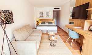 Et hotelværelse med en sofa, en dobbeltseng, et skrivebord med en stol og et fjernsyn. (AI-genereret tekst)