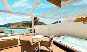 Terrasse med bord, stole, boblebad og udsigt over stranden og havet. (AI-genereret tekst)