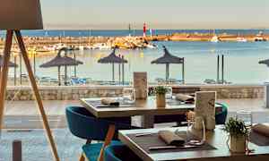 Udsigt fra en restaurant mod en strand med parasoller og liggestole samt en lystbådehavn med både. (AI-genereret tekst)