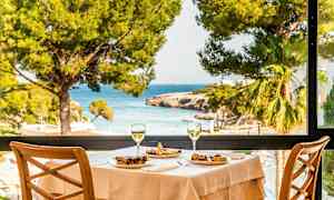 Et dækket bord med mad og to glas vin med udsigt over havet gennem et stort vindue. (AI-genereret tekst)