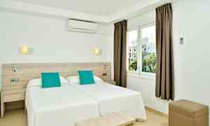 Et hotelværelse med to enkeltsenge ved siden af hinanden, hvid indretning og turkise puder, samt et vindue med udsigt. (AI-genereret tekst)