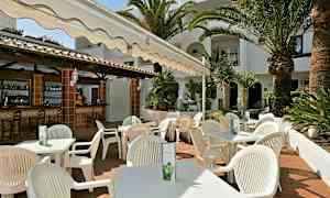 En udendørs servering med hvide stole og borde under en markise, omgivet af palmer og grønne områder. (AI-genereret tekst)