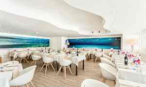 En moderne restaurant med hvide stole og borde samt et stort undervandsmaleri på væggen. (AI-genereret tekst)