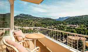 Udendørsmøbler på en altan med udsigt over en frodig dal og bjerge i baggrunden. (AI-genereret tekst)