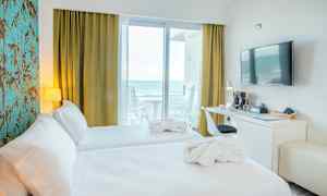 Hotelværelse med to senge, skrivebord, væg-TV og havudsigt fra altanen. (AI-genereret tekst)