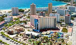 Luftfoto af en kystby med hotelbygninger, strand og et forlystelsesområde. (AI-genereret tekst)