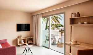 Hotelværelse med siddeområde, TV, bord og altan med udsigt til palmer. (AI-genereret tekst)