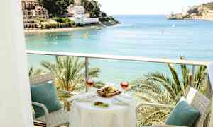 En altan med bord og stole, med udsigt over en bugt med palmer og bygninger i baggrunden. (AI-genereret tekst)