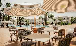 Udendørs poolområde med liggestole, parasoller og borde med stole. (AI-genereret tekst)