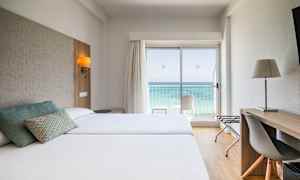 Hotelværelse med to senge, skrivebord og udsigt over havet gennem en glasdør. (AI-genereret tekst)