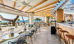 En udendørs bar med siddepladser, havet synligt i baggrunden. (AI-genereret tekst)