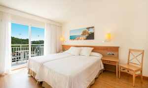 Et hotelværelse med to enkeltsenge, en altan og et landskabsfoto på væggen. (AI-genereret tekst)