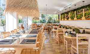 Restaurant med træborde, rottingstole og dekorative lysarmaturer. (AI-genereret tekst)