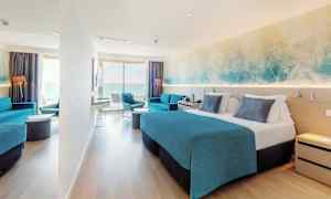 Et hotelværelse med dobbeltseng, blå indretning og en siddegruppe. Et stort vindue giver udsigt over havet. (AI-genereret tekst)