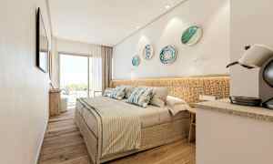 Et moderne hotelværelse med en dobbeltseng, dekorative pyntefade på væggen, en kaffemaskine og store glasdøre, der fører til en altan. (AI-genereret tekst)