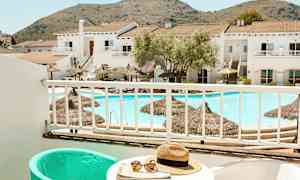 Udsigt fra en balkon til en pool og bygninger med bjerge i baggrunden. (AI-genereret tekst)