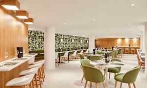 En restaurantinteriør med grønmalede stole og en tapetseret væg med plantemønster. (AI-genereret tekst)