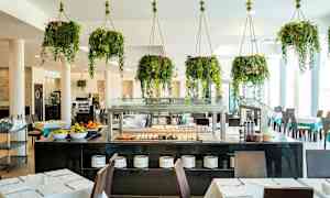 Restaurant med borde, stole og buffet samt hængende grønne planter. (AI-genereret tekst)