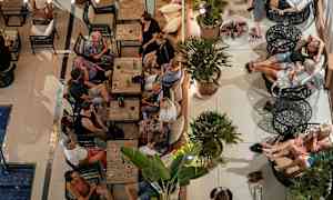 En gruppe mennesker sidder ved borde og sofaer i en udendørs lounge. (AI-genereret tekst)