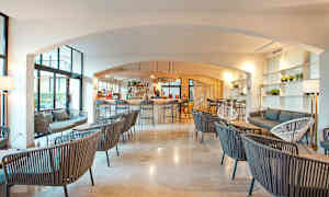 Interiør af en moderne lounge med bar, hvor flere siddegrupper er opstillet med stole og sofaer i et lyst og luftigt rum. (AI-genereret tekst)