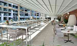 Et moderne og lyst indrettet terrasse- eller restaurantområde med glasvægge, rækker af borde og stole samt dekorative planter. (AI-genereret tekst)