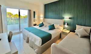 Et hotelværelse med en dobbeltseng, en sofa, et skrivebord og et vindue med udsigt til vegetation. (AI-genereret tekst)