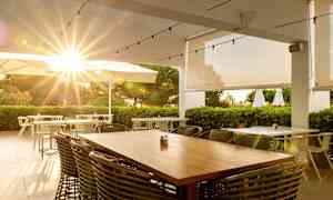 Udendørrestaurant med solstråler gennem parasoller og grønt. (AI-genereret tekst)