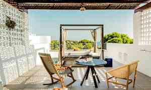 En terrasse med to stole og et lille bord samt en daybed med udsigt over grønt og hav. (AI-genereret tekst)