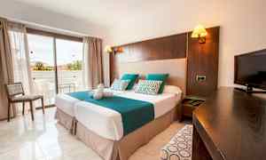 Et hotelværelse med to enkeltsenge, et tv og en altan i baggrunden. (AI-genereret tekst)