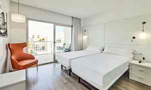 Et lyst og moderne hotelværelse med to enkeltsenge, en orange lænestol og et glasvindue, der fører ud til en altan. (AI-genereret tekst)