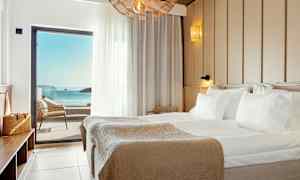 Et hotelværelse med en stor seng og havudsigt gennem en altandør. (AI-genereret tekst)