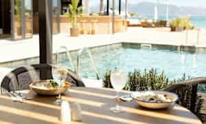 Spisebord ved siden af poolen med to retter og drikkevarer. (AI-genereret tekst)