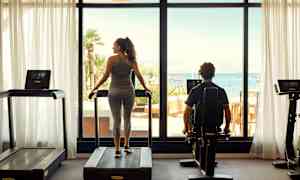 Fitnesscenter med udsigt over havet gennem store vinduer. (AI-genereret tekst)