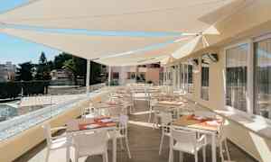 En terrasse med borde og stole under solafskærmning. (AI-genereret tekst)